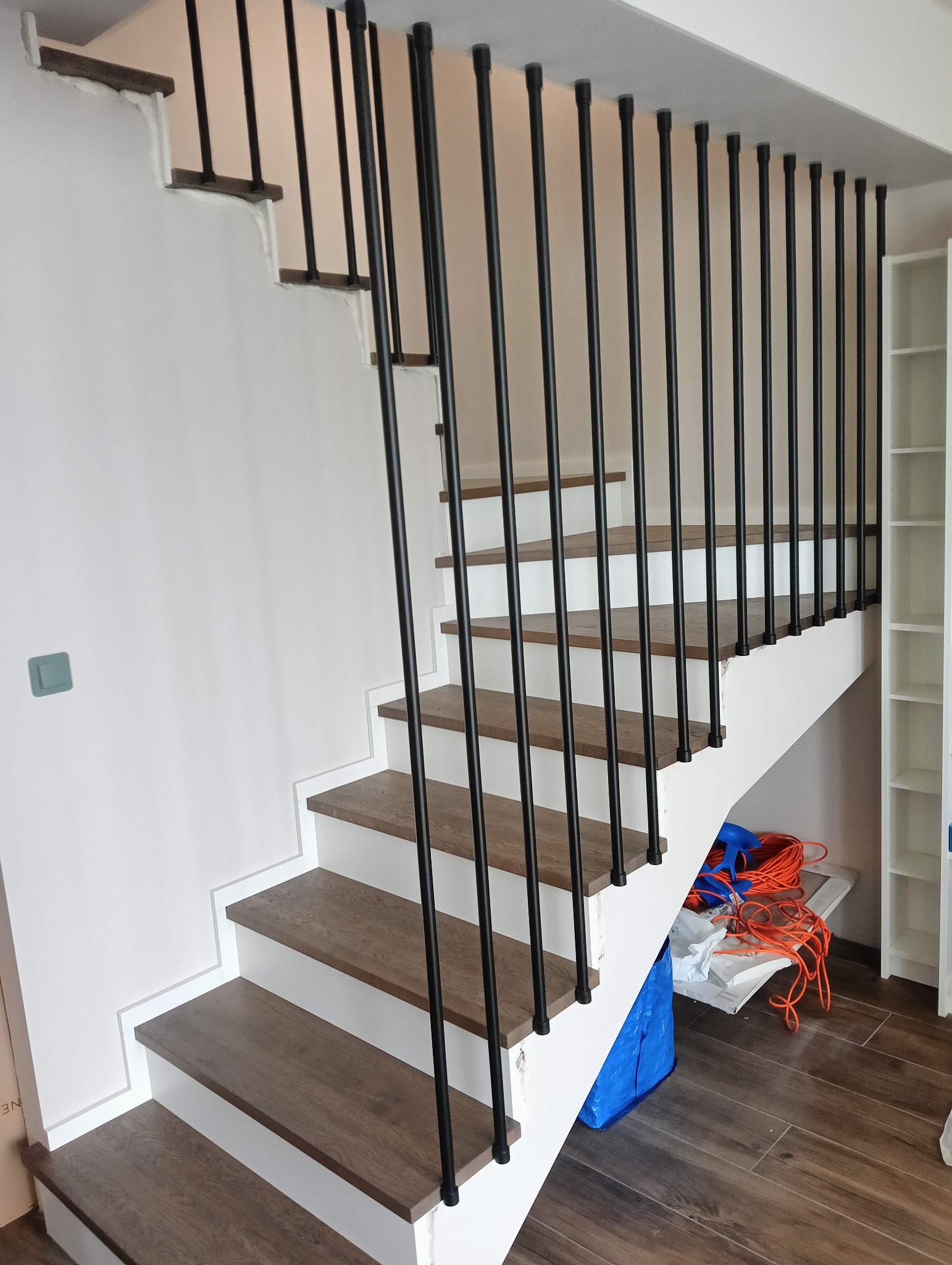 Nowoczesne schody z drewnianymi stopniami i czarną, metalową balustradą. Białe boki schodów, brązowe stopnie, widok z dołu na górę, minimalistyczny styl.