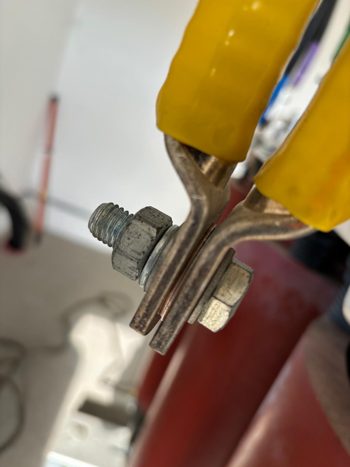 Złącze elektryczne z miedzianymi elementami, śrubami i nakrętkami, zabezpieczone żółtą izolacją, uchwycone w zbliżeniu.