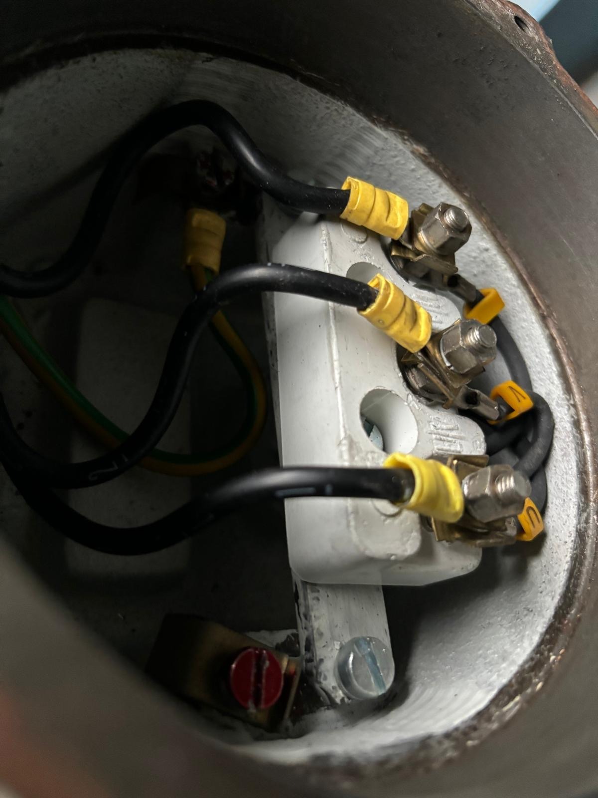 Wnętrze puszki elektrycznej z podłączonymi przewodami zabezpieczonymi żółtymi tulejkami i przykręconymi śrubami, widoczne elementy instalacji.