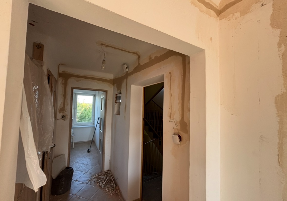 Korytarz w trakcie remontu: świeżo położona gładź szpachlowa na ścianach, widoczne kable elektryczne wystające ze ściany, przygotowane do montażu gniazdka.