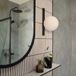 ALZA STUDIO Alicja Zapolna - Nowoczesna łazienka z okrągłym lustrem w czarnej ramie, oświetleniem kulistym i minimalistycznymi akcentami roślinnymi na półce z płytek.