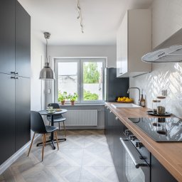 ALZA STUDIO Alicja Zapolna - Nowoczesna kuchnia z czarnymi szafkami, drewnianym blatem i białymi płytkami ułożonymi w jodełkę. Stół z krzesłami przy oknie, nad nim lampa. Jasne, przestronne wnętrze.