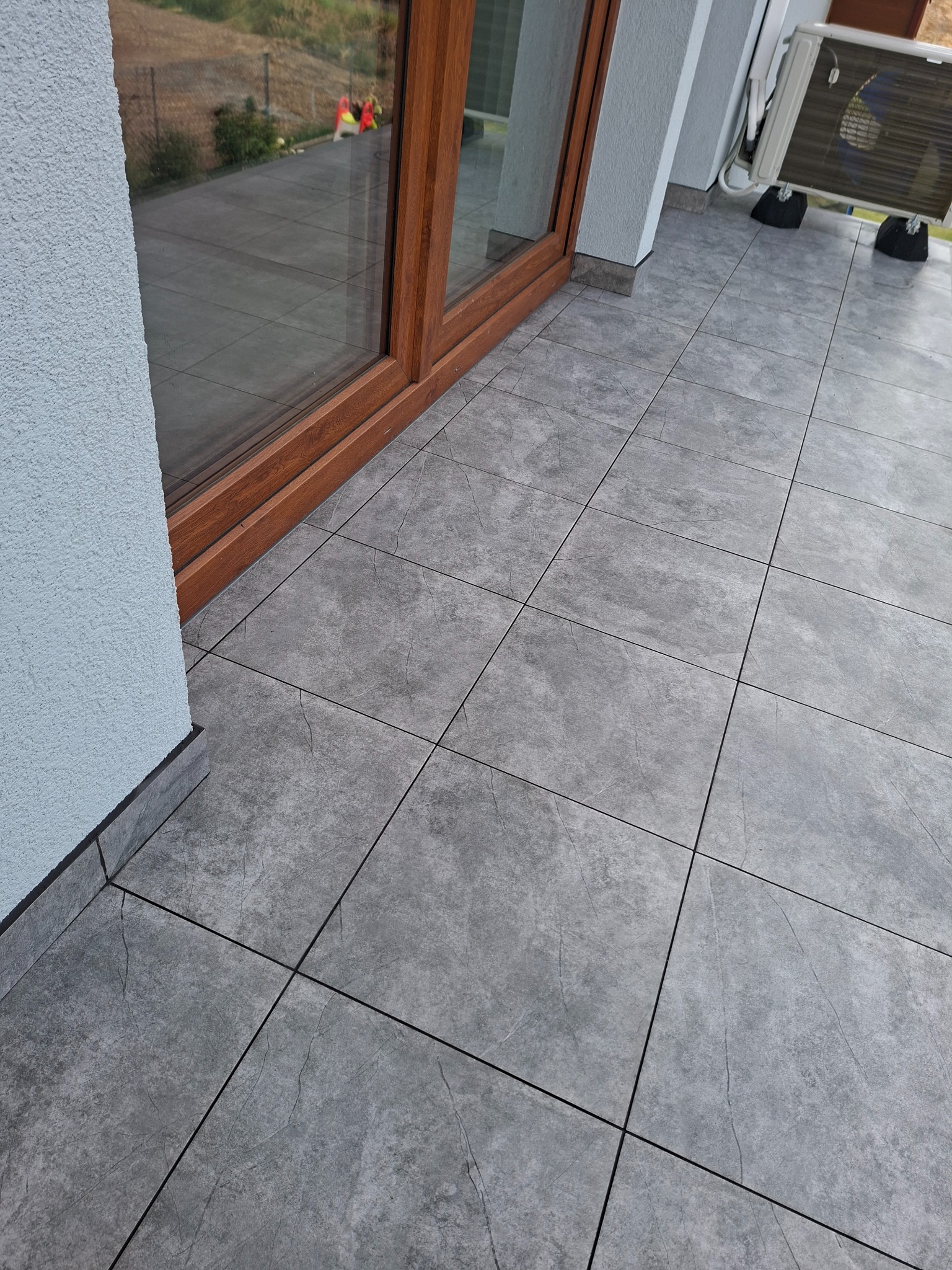 Szare płytki gresowe na balkonie, widok z góry, z oknem balkonowym i klimatyzatorem w tle. Minimalistyczny design, nowoczesne wykończenie.