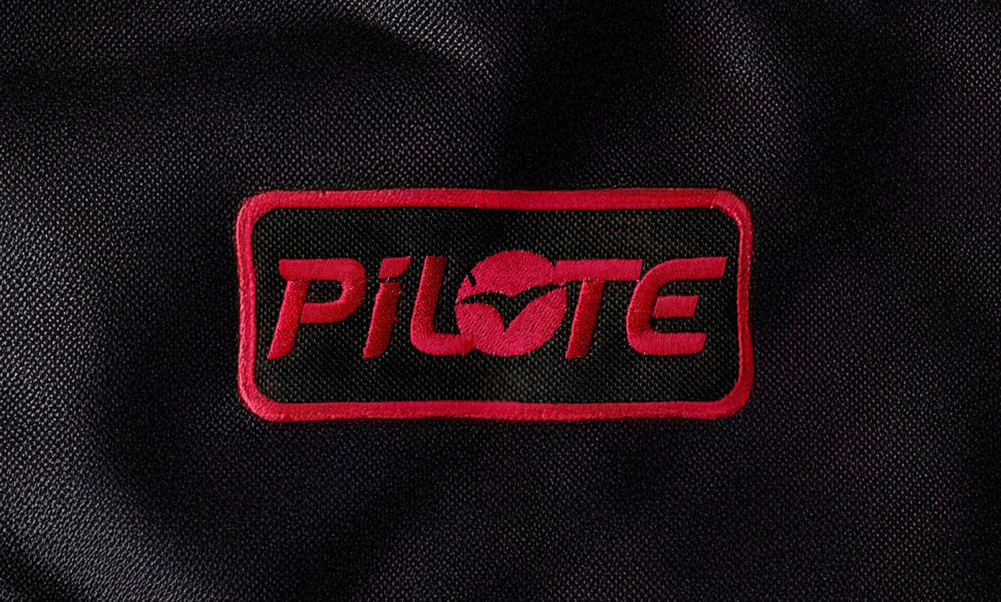 Czerwony, haftowany napis 'PILOTE' na czarnym materiale. Precyzyjne wykonanie w Miedzianej Górze. Detal odzieży roboczej lub firmowej.