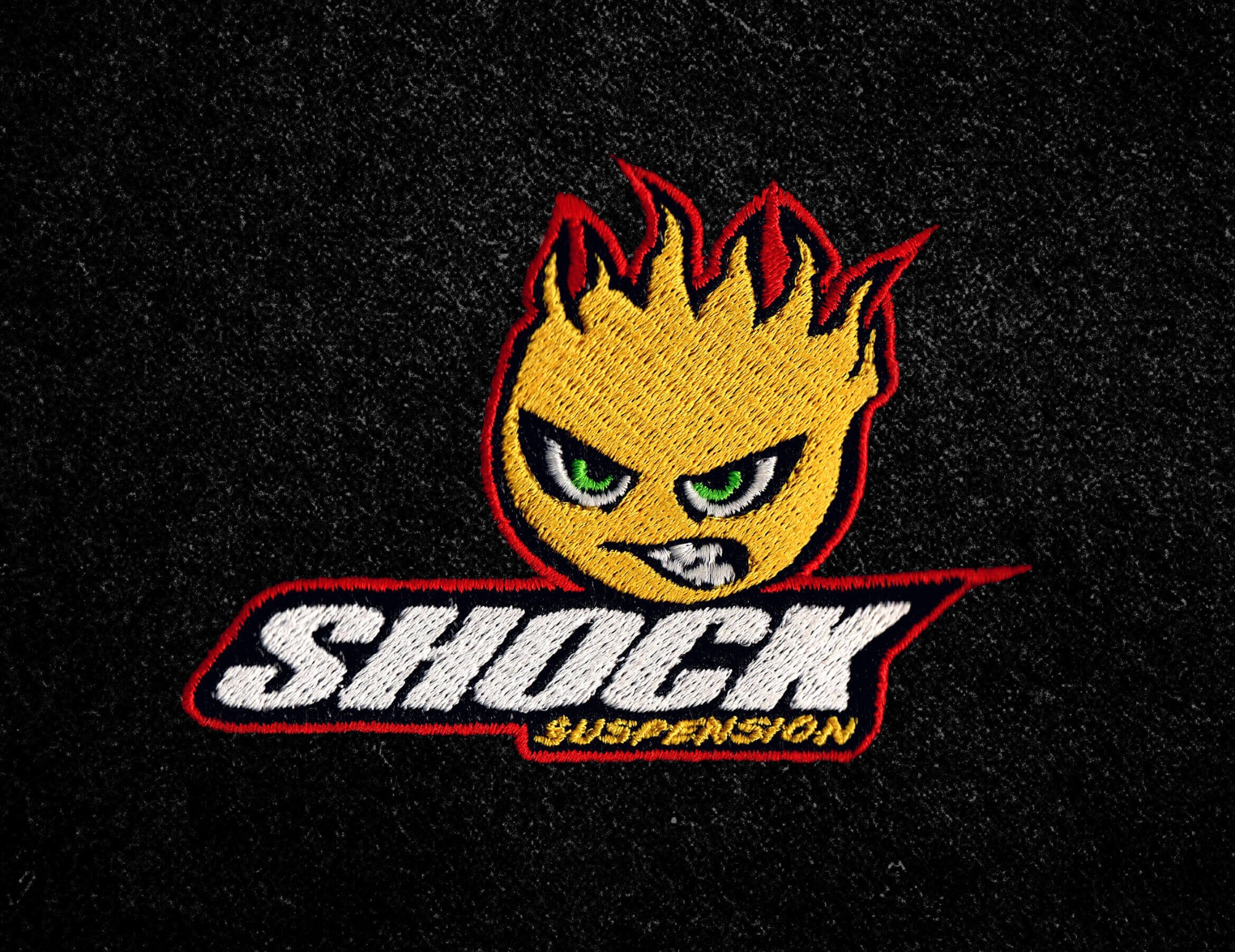 Emblemat haftowany na czarnym tle z motywem płomiennej głowy i napisem 'SHOCK SUSPENSION' w białej i czerwonej nici. Precyzyjne detale haftu.