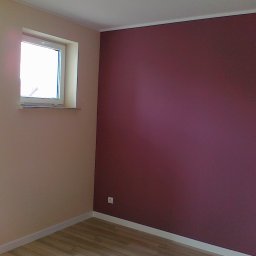 House color renovation - Pokój po malowaniu: ściana w odcieniu burgundu, druga w beżu, okno z białymi ramami, jasna podłoga. Widoczny kontakt elektryczny.