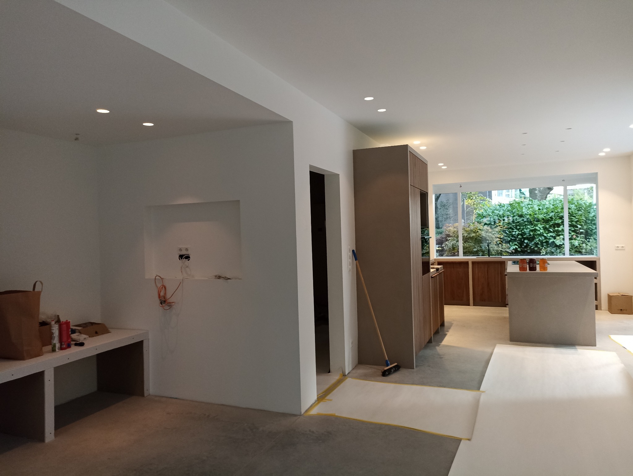 Wnętrze w trakcie prac wykończeniowych: widoczne przygotowane ściany, instalacja elektryczna, zabezpieczona podłoga i meble kuchenne w nowoczesnym stylu.