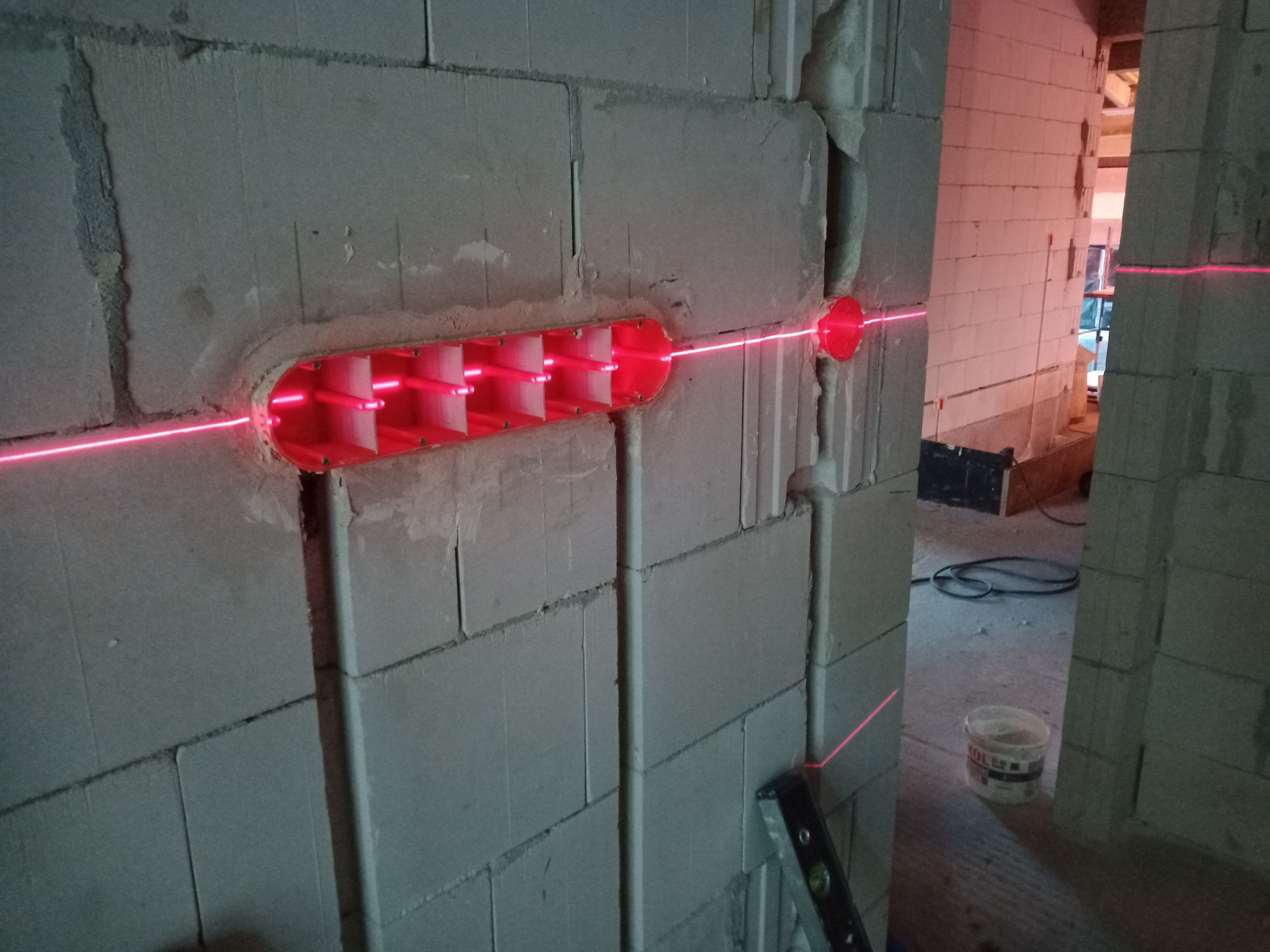 Wykucie bruzdy w ścianie z betonu komórkowego pod instalację, widoczny laser krzyżowy wyznaczający linię, wnętrze budynku w tle.