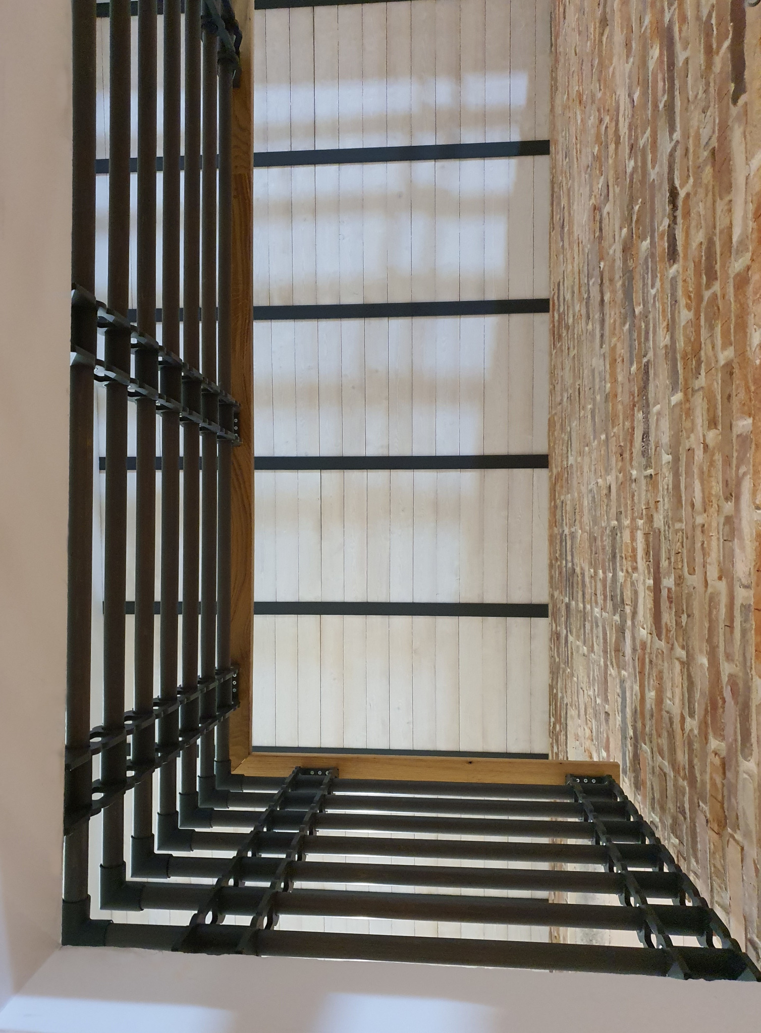 Fragment wnętrza z odsłoniętą instalacją wentylacyjną, sufit z drewnianymi belkami i fragment ceglanej ściany. Widok z dołu, perspektywa zbieżna.