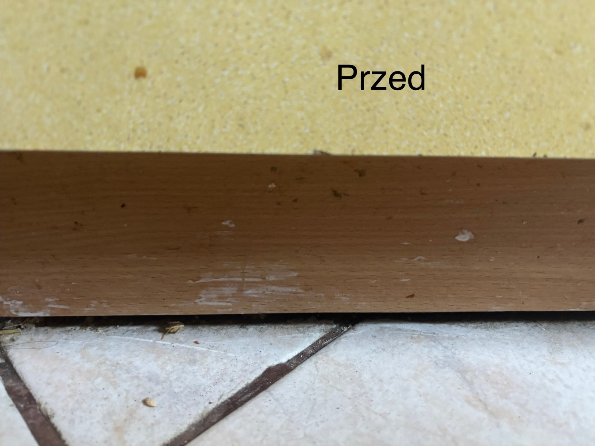 Brudna podłoga i listwa przypodłogowa z tekstem 'Przed'. Widoczne zabrudzenia, kurz i plamy na powierzchniach przed sprzątaniem.