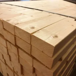 Stos tarcicy budowlanej z widocznymi słojami drewna i detalami cięcia, zabezpieczony taśmą. Jasne drewno w magazynie.