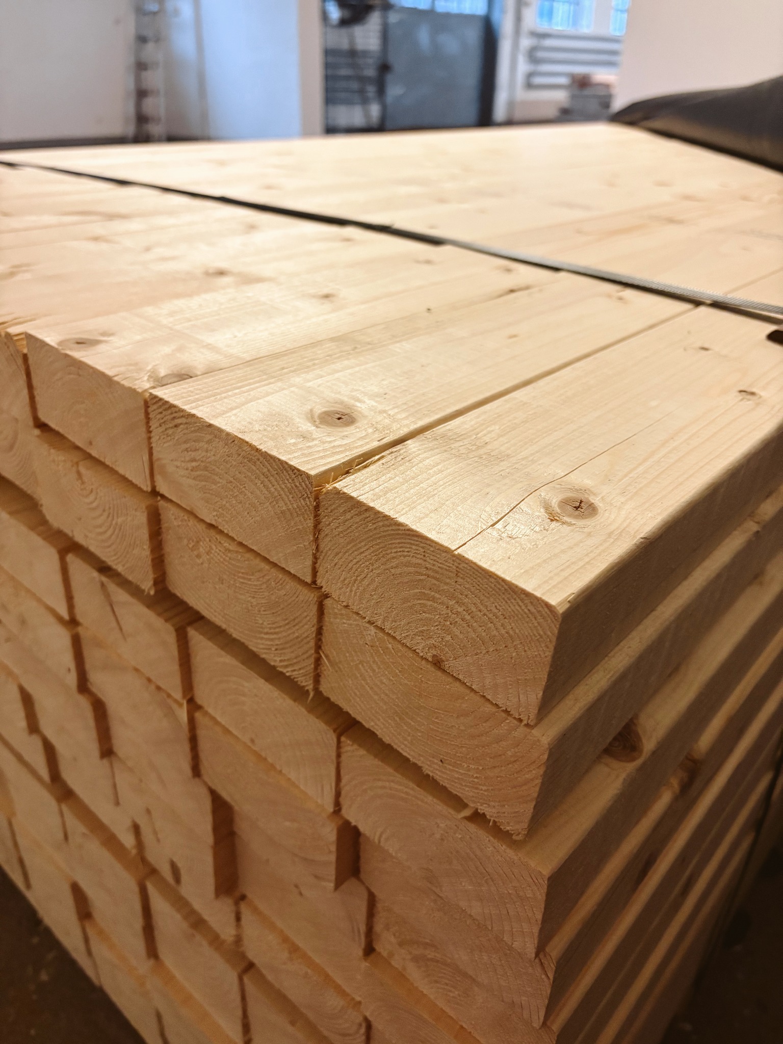 Stos tarcicy budowlanej z widocznymi słojami drewna i detalami cięcia, zabezpieczony taśmą. Jasne drewno w magazynie.