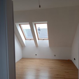 CraftPRO - Poddasze z drewnianą podłogą i oknami dachowymi, widok przez otwarte drzwi. W tle widoczny fragment dachu przez okna.