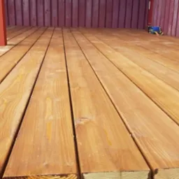 Jasne, świeżo położone deski tarasowe z widocznym rysunkiem drewna, narzędzia pracy w tle. Widok z niskiej perspektywy, ukazujący strukturę drewna.