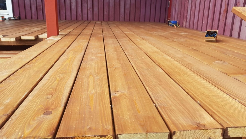 Jasne, świeżo położone deski tarasowe z widocznym rysunkiem drewna, narzędzia pracy w tle. Widok z niskiej perspektywy, ukazujący strukturę drewna.