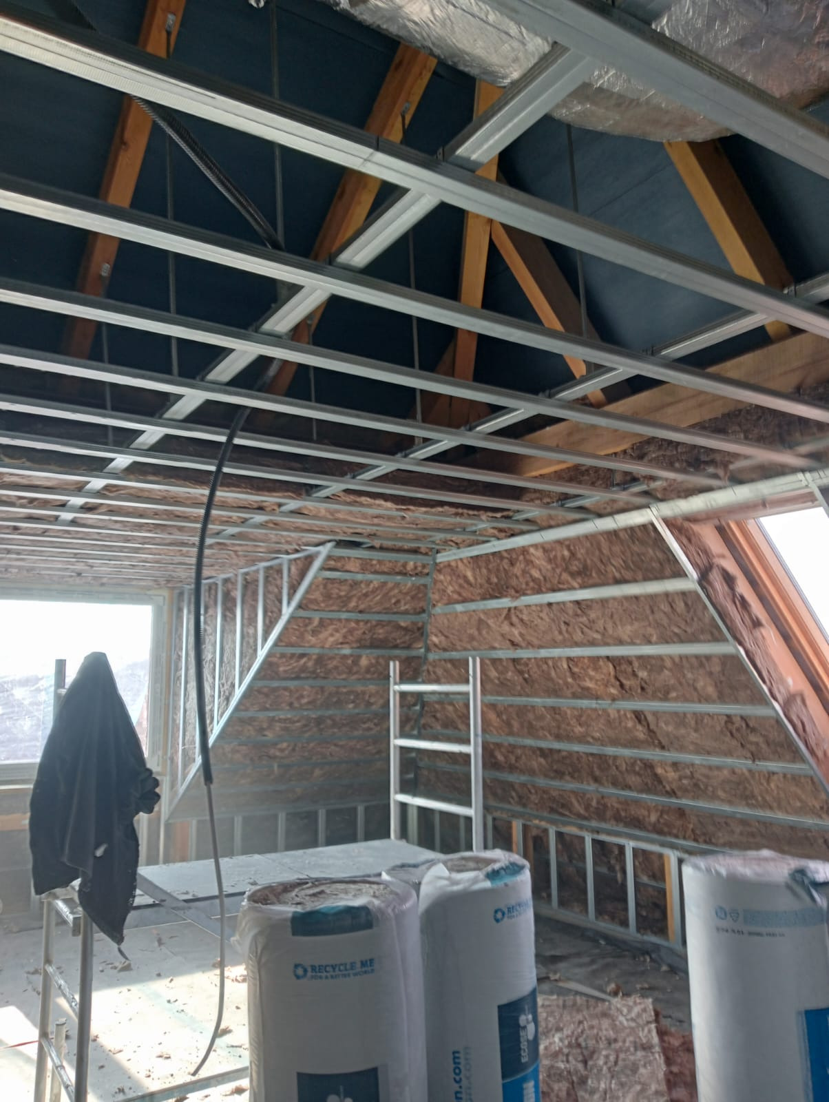 Montaż stelaża pod płyty gipsowe na poddaszu, widoczna izolacja ścian i stropu. Metalowe profile tworzą konstrukcję pod zabudowę.