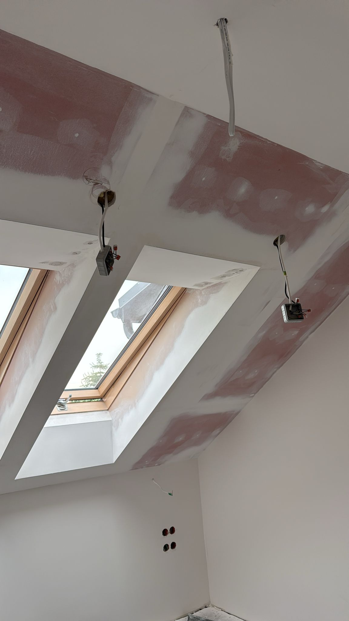 Poddasze z oknami dachowymi w trakcie szpachlowania. Widoczne otwory na oświetlenie i ślady po szpachli na ścianach oraz suficie.