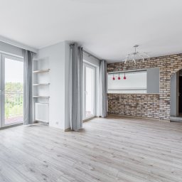 Freedom - Przemysław Baran - Jasne, przestronne wnętrze po remoncie w Markach: parkiet, ceglana ściana, okna balkonowe z widokiem na zieleń. Nowoczesne oświetlenie i minimalistyczne półki.