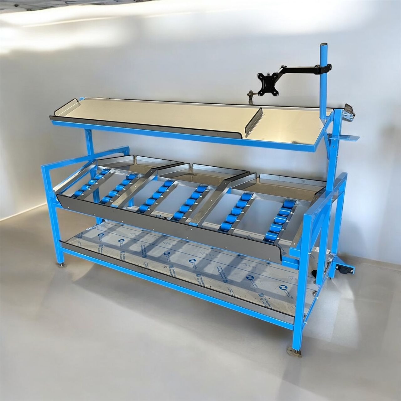 Niebieska, metalowa konstrukcja regału z rolkami i blatem, przeznaczona do zastosowań przemysłowych, ustawiona w jasnym pomieszczeniu.
