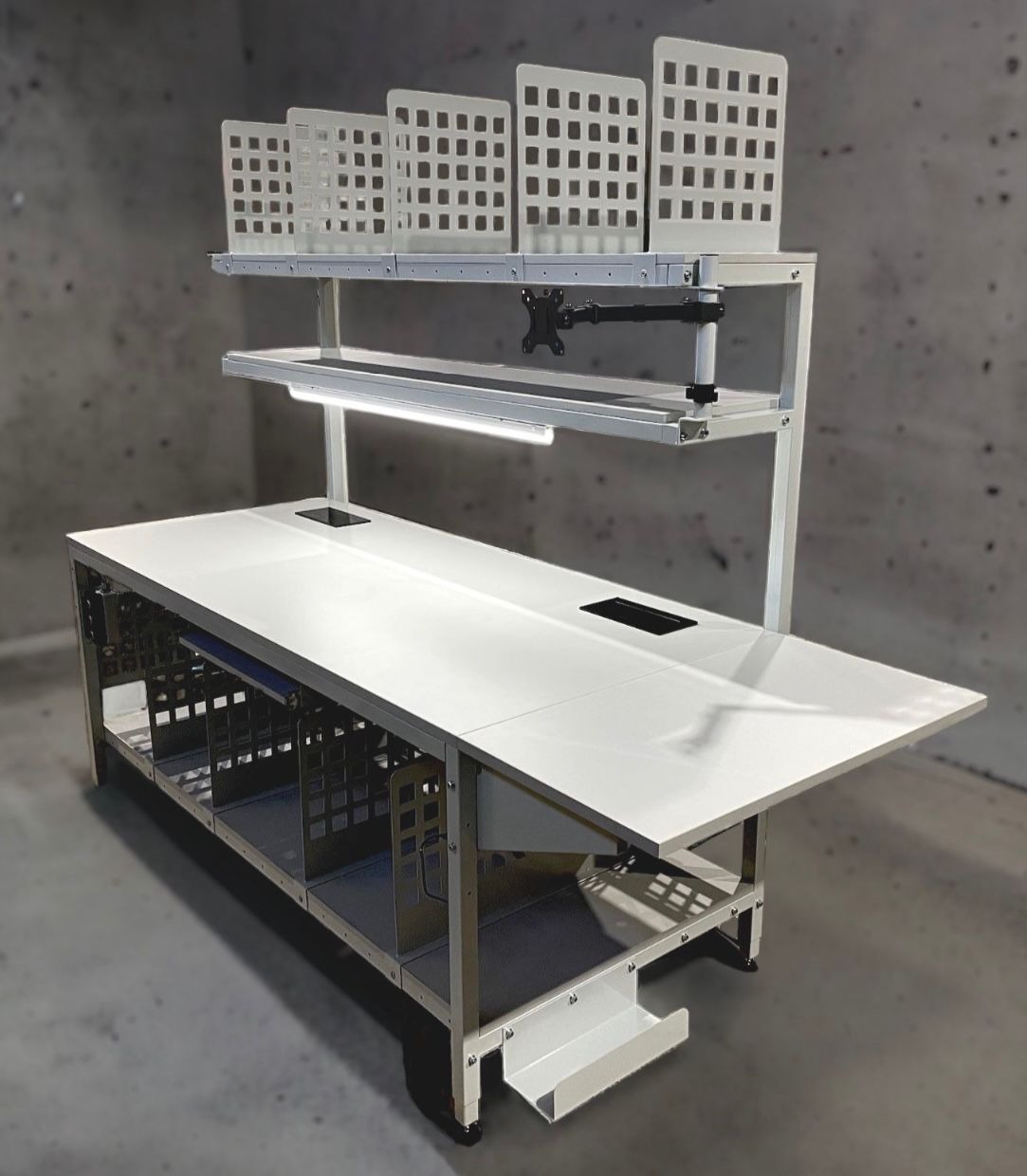 Ergonomiczne stanowisko robocze: biały stół z metalową konstrukcją, oświetleniem LED i uchwytem na monitor. Dodatkowe panele z perforacją nad blatem.