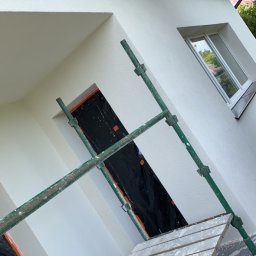 Sebastian Ślusarczyk - Biała elewacja domu po renowacji w Szprotawie, widoczna z poziomu rusztowania. Okno i otwór zabezpieczone folią malarską.