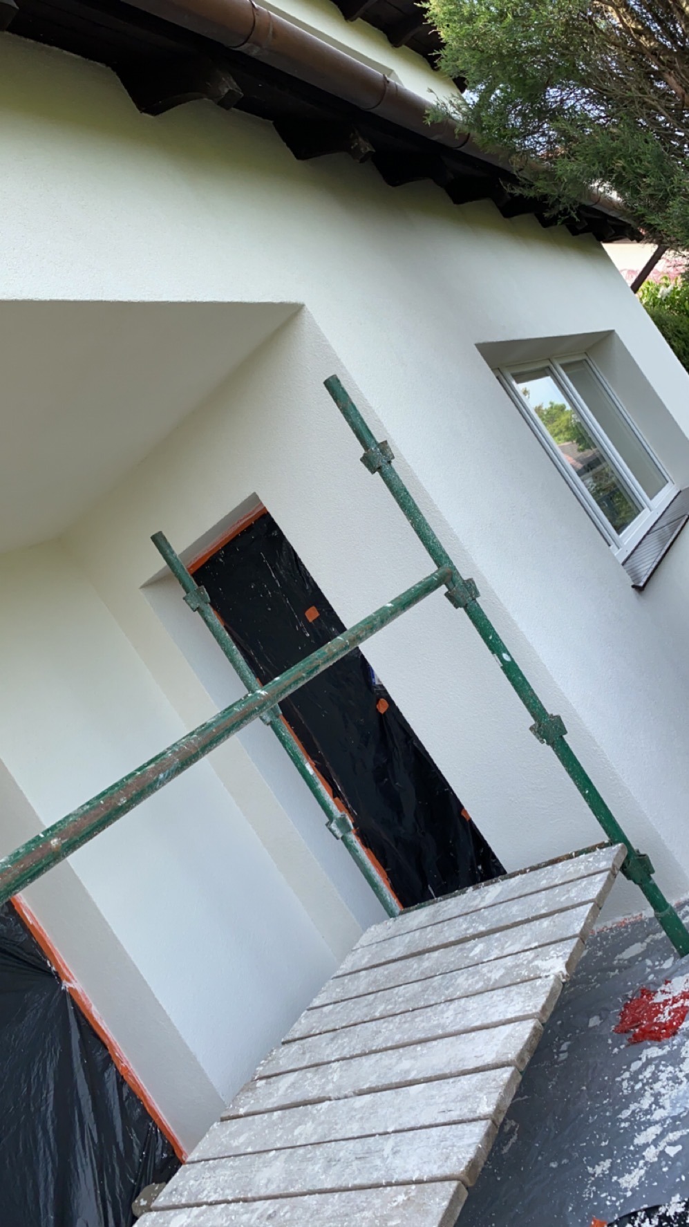 Biała elewacja domu po renowacji w Szprotawie, widoczna z poziomu rusztowania. Okno i otwór zabezpieczone folią malarską.