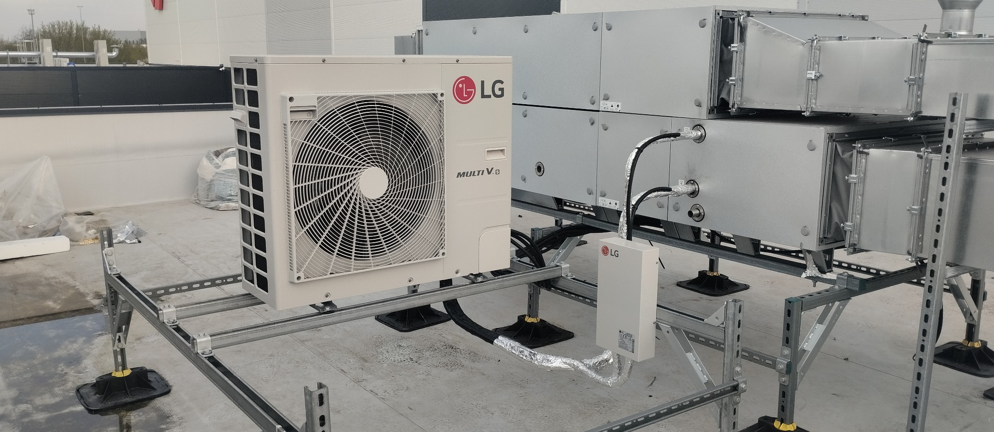 Instalacja klimatyzacji LG Multi V na dachu budynku. Widoczne jednostki zewnętrzne i kanały wentylacyjne, całość zamontowana na metalowej konstrukcji wsporczej.