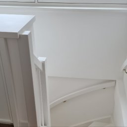 Kamil Mikołajski usługi ogólnobudowlane - Białe, drewniane schody kręte z poręczą i szafką z złotymi uchwytami, w jasnym wnętrzu. Widok z góry na dół.