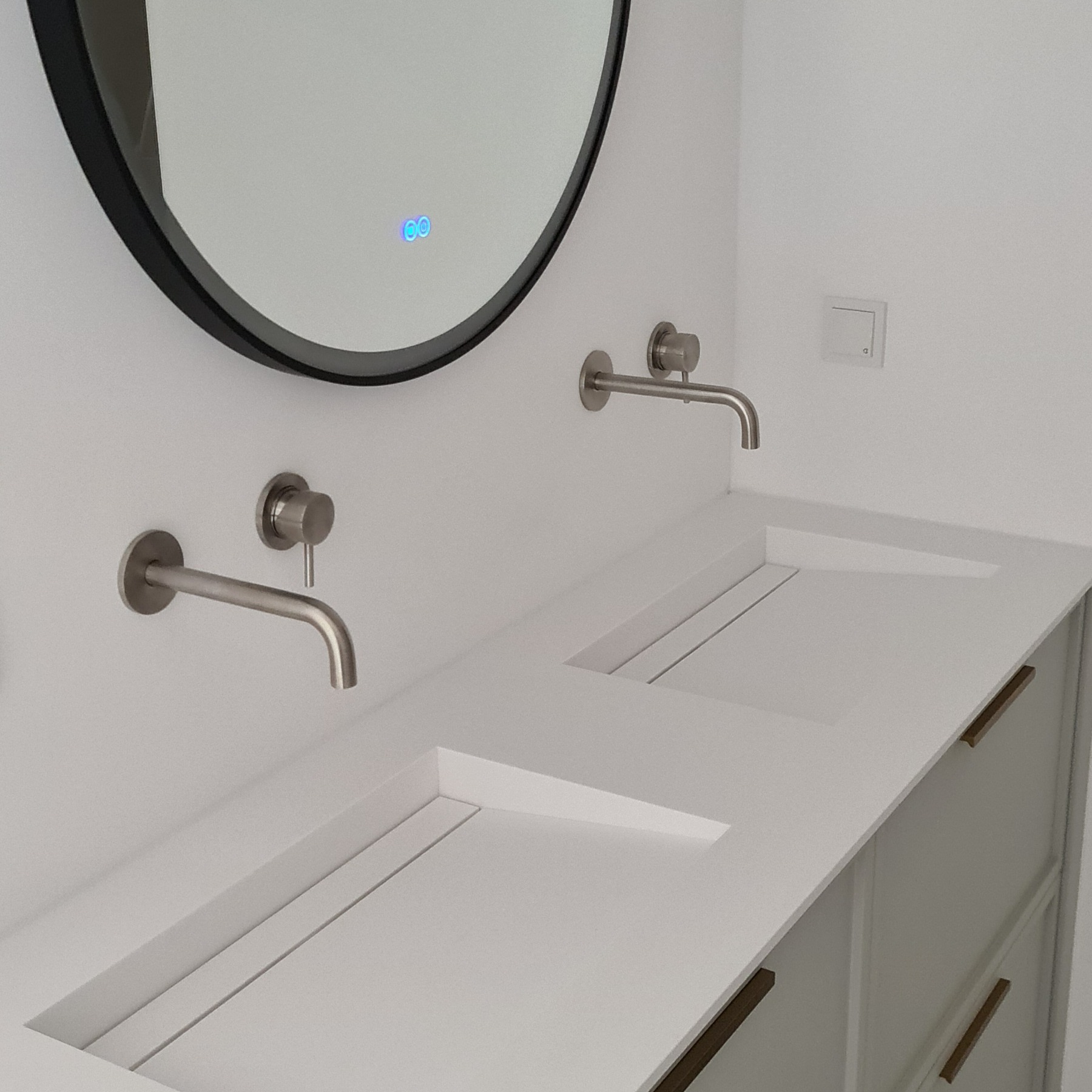 Nowoczesna łazienka z podwójną umywalką wpuszczoną w blat, okrągłe lustro z podświetleniem LED i minimalistyczną armaturą w kolorze szczotkowanego niklu.