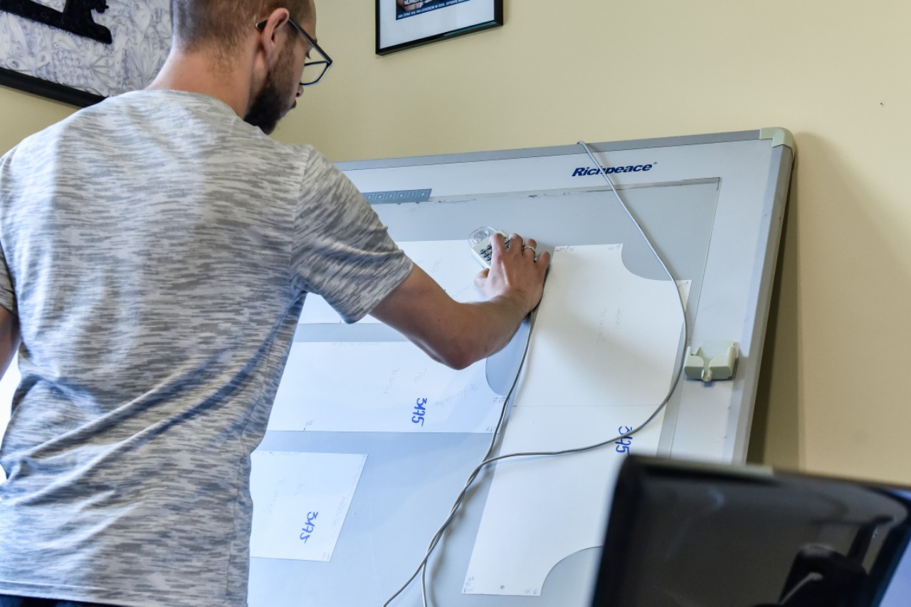 Projektant odzieży w trakcie pracy nad szablonem na podświetlanym stole kreślarskim Richpeace, precyzyjnie odmierzając wymiary.