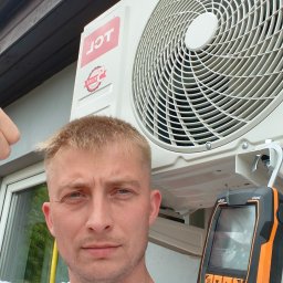 Ariel Paszczak Klimatyzacja - Instalator klimatyzacji TCL daje kciuk w górę obok zamontowanego urządzenia na elewacji, trzymając miernik elektroniczny. Widok z dołu na klimatyzator.