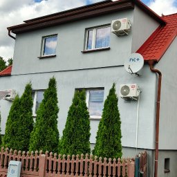 Ariel Paszczak Klimatyzacja - Szary dom jednorodzinny z czerwonym dachem. Na ścianach zamontowane klimatyzatory TCL i antena satelitarna nc+. W tle widoczne panele fotowoltaiczne.