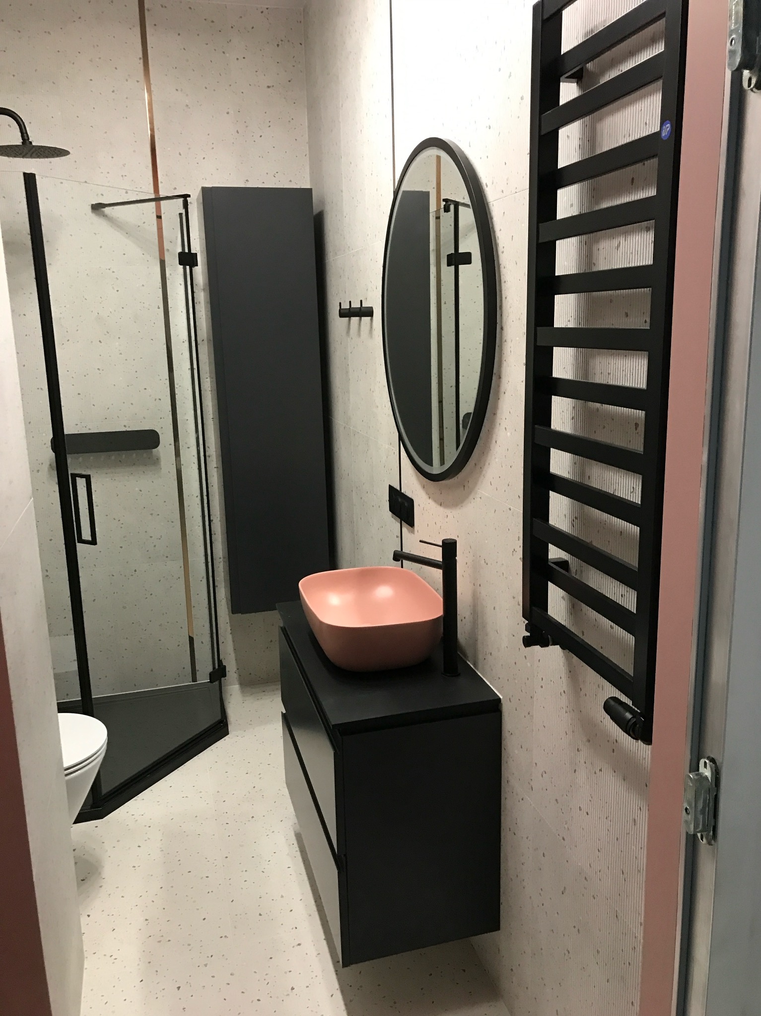 Nowoczesna łazienka z kabiną prysznicową typu walk-in, umywalką w kolorze pudrowego różu i czarnymi akcentami: grzejnik, armatura, rama lustra.
