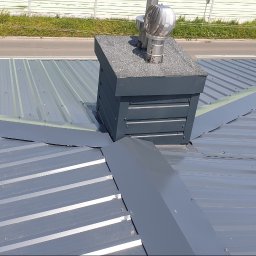 KedarInwest - Szary dach z blachy trapezowej, komin z blachy i wentylacją, obróbki blacharskie. Detal dachu z blachy na zewnątrz budynku. Widok z góry na nowy dach.