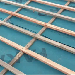 Konstrukcja drewniana dachu z membraną hydroizolacyjną w kolorze turkusowym, tworząca siatkę. Widoczne elementy mocujące. Ujęcie z góry.