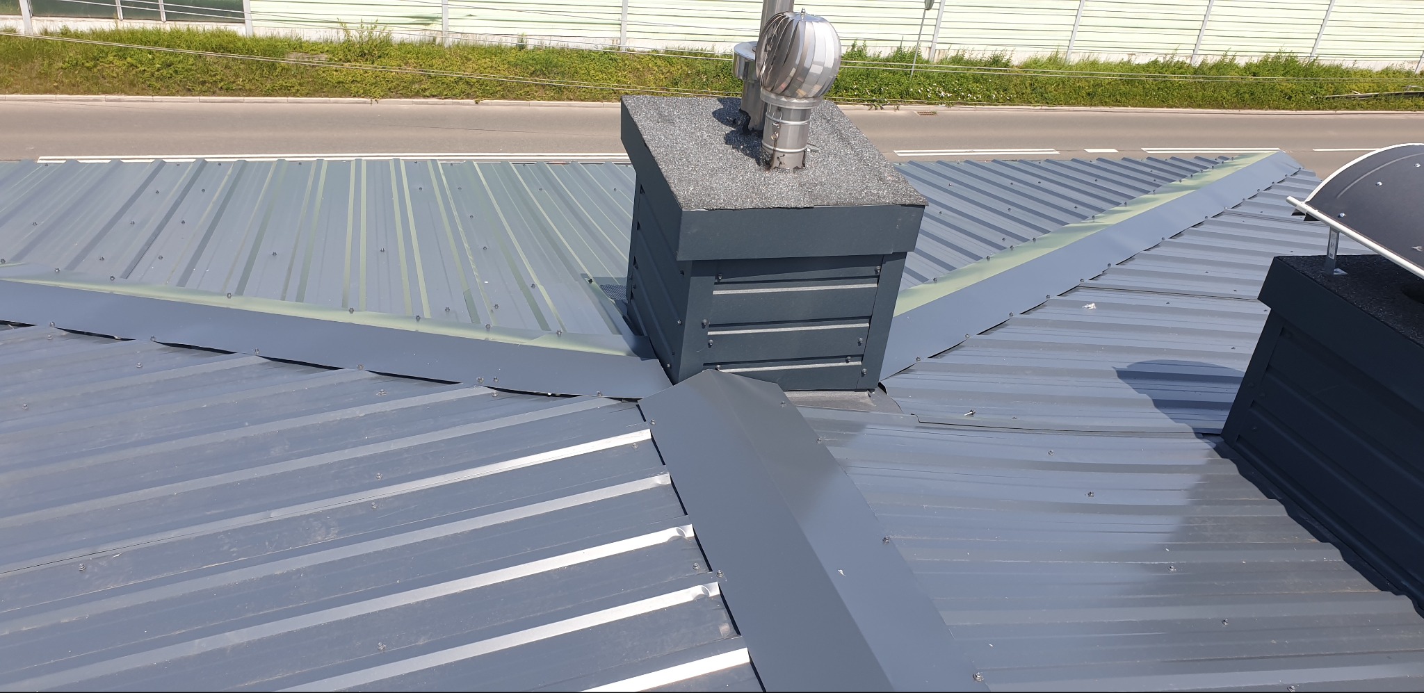 Szary dach z blachy trapezowej, komin z blachy i wentylacją, obróbki blacharskie. Detal dachu z blachy na zewnątrz budynku. Widok z góry na nowy dach.