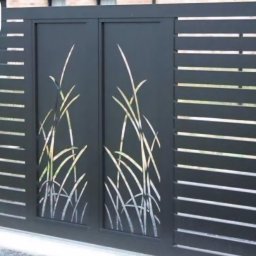 Usługi Spawalnicze Krzysztof Skorniak - Nowoczesna, przesuwna brama wjazdowa z metalu, w kolorze grafitowym. Dekoracyjny motyw roślinny wycięty laserowo. Poziome lamele po bokach bramy.
