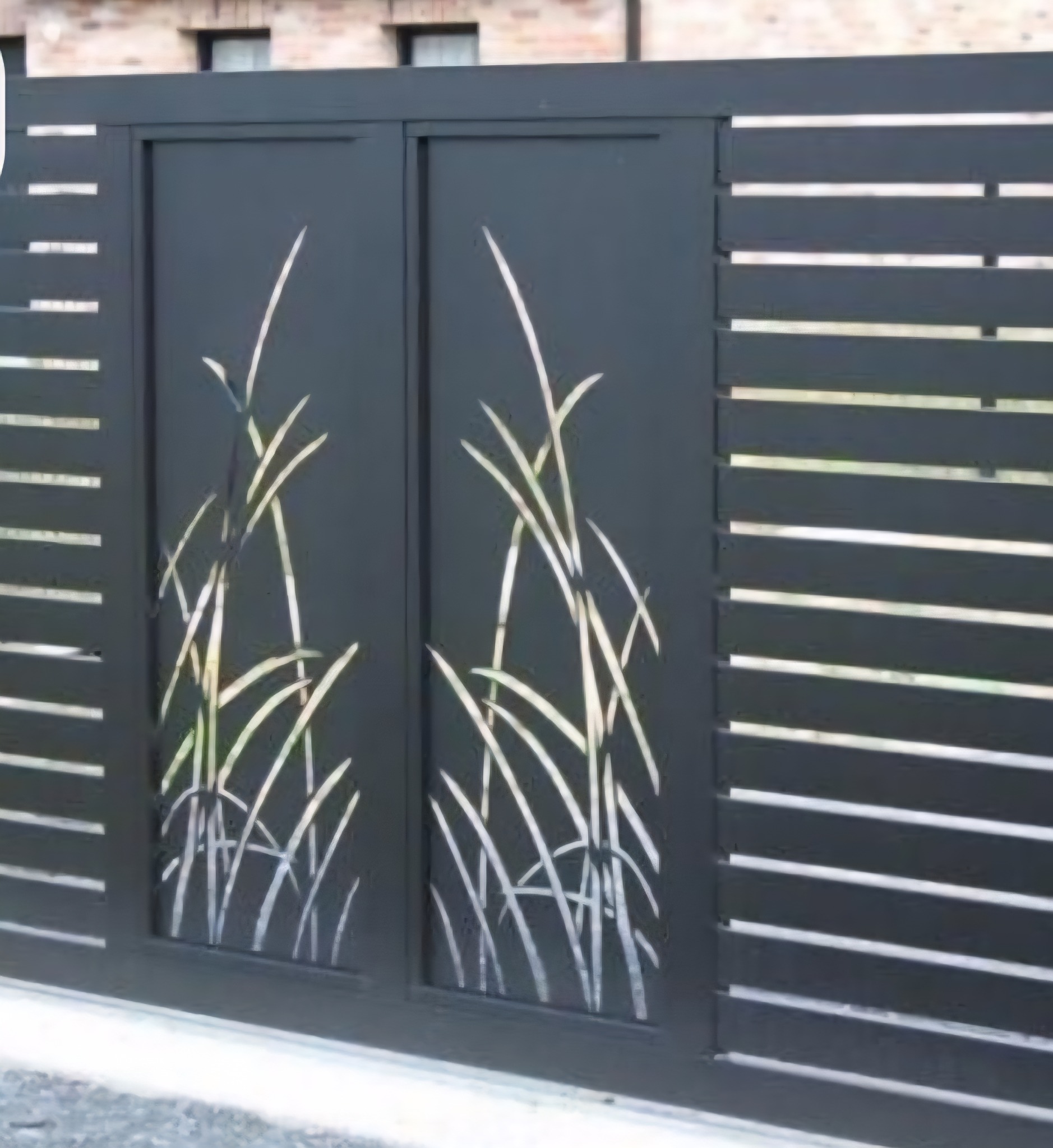 Nowoczesna, przesuwna brama wjazdowa z metalu, w kolorze grafitowym. Dekoracyjny motyw roślinny wycięty laserowo. Poziome lamele po bokach bramy.