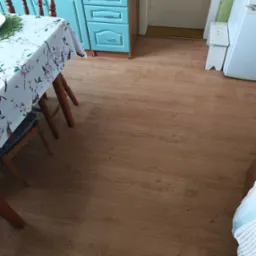 Kuchnia po remoncie: świeżo ułożona podłoga z paneli imitujących drewno, widok na fragment stołu i błękitne szafki kuchenne.