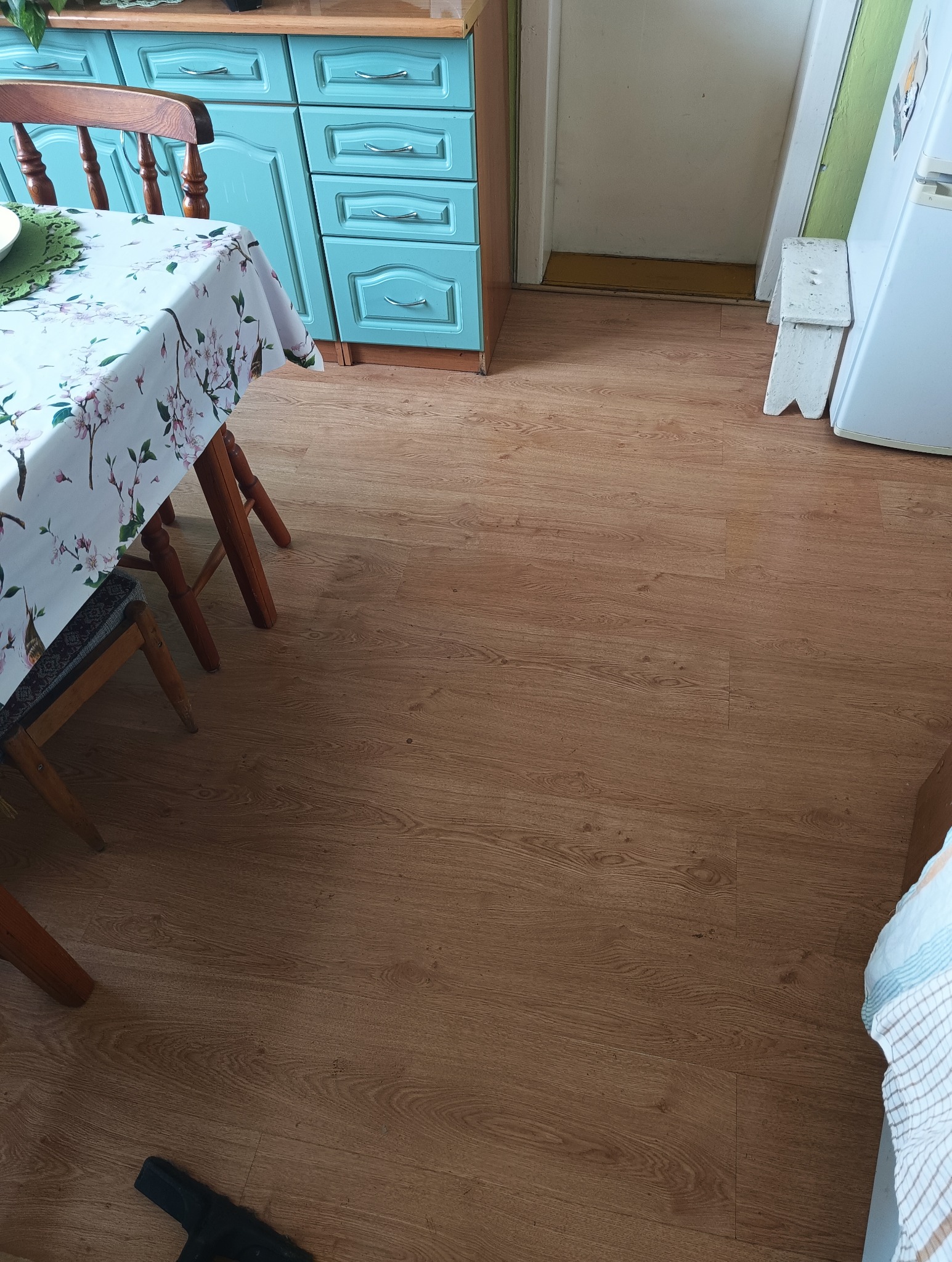 Kuchnia po remoncie: świeżo ułożona podłoga z paneli imitujących drewno, widok na fragment stołu i błękitne szafki kuchenne.