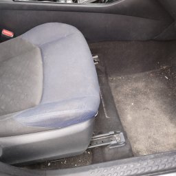 CZYSTA ROBOTA-EKIPA NA BŁYSK - Brudne, zaniedbane wnętrze samochodu: fotel z plamami i zabrudzeniami, zanieczyszczona podłoga. Widoczne okruchy i kurz. Potrzeba gruntownego czyszczenia.