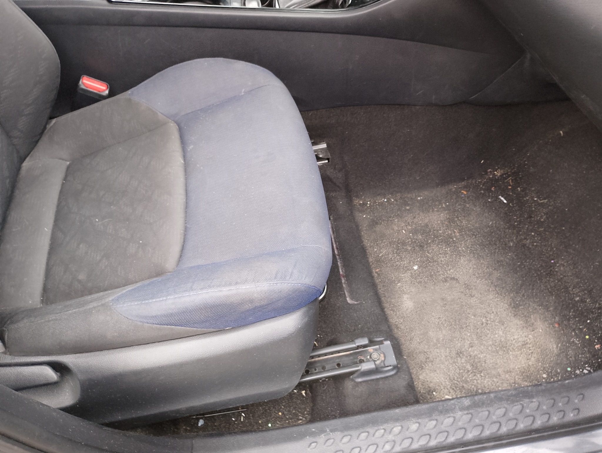 Brudne, zaniedbane wnętrze samochodu: fotel z plamami i zabrudzeniami, zanieczyszczona podłoga. Widoczne okruchy i kurz. Potrzeba gruntownego czyszczenia.