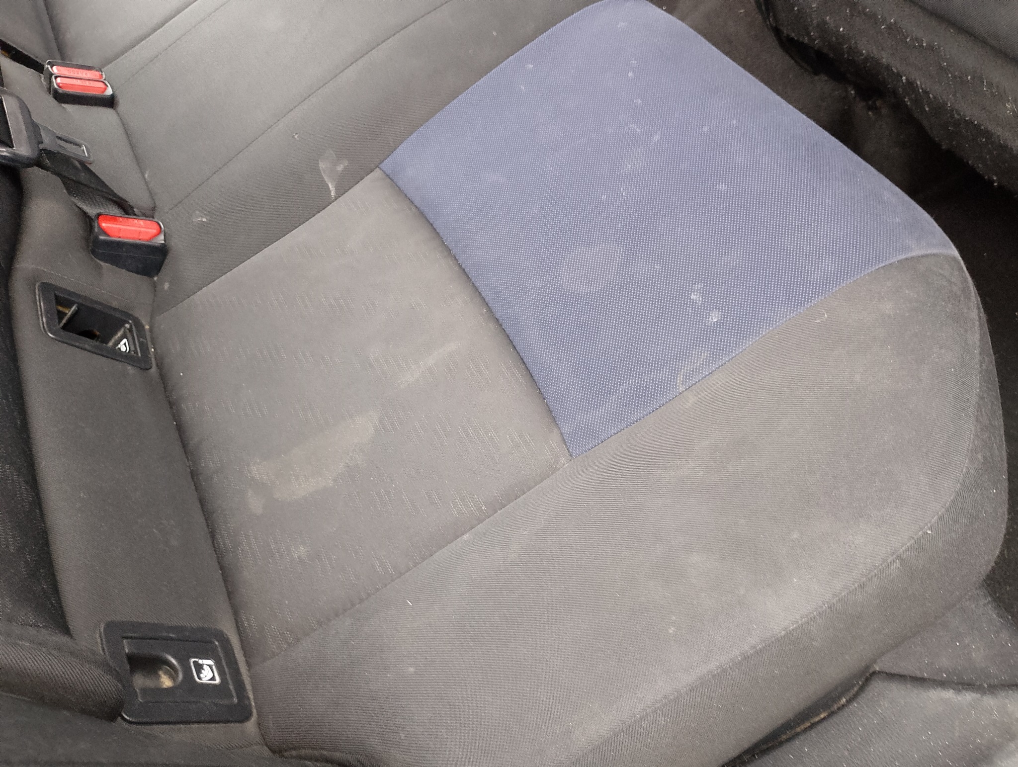 Tapicerka samochodowa z plamami i zabrudzeniami, widoczne mocowania pasów bezpieczeństwa. Wymaga czyszczenia.