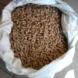 Worek wypełniony jasnymi, drobnymi granulkami paliwa stałego, prawdopodobnie biomasy, z widoczną fakturą materiału worka.