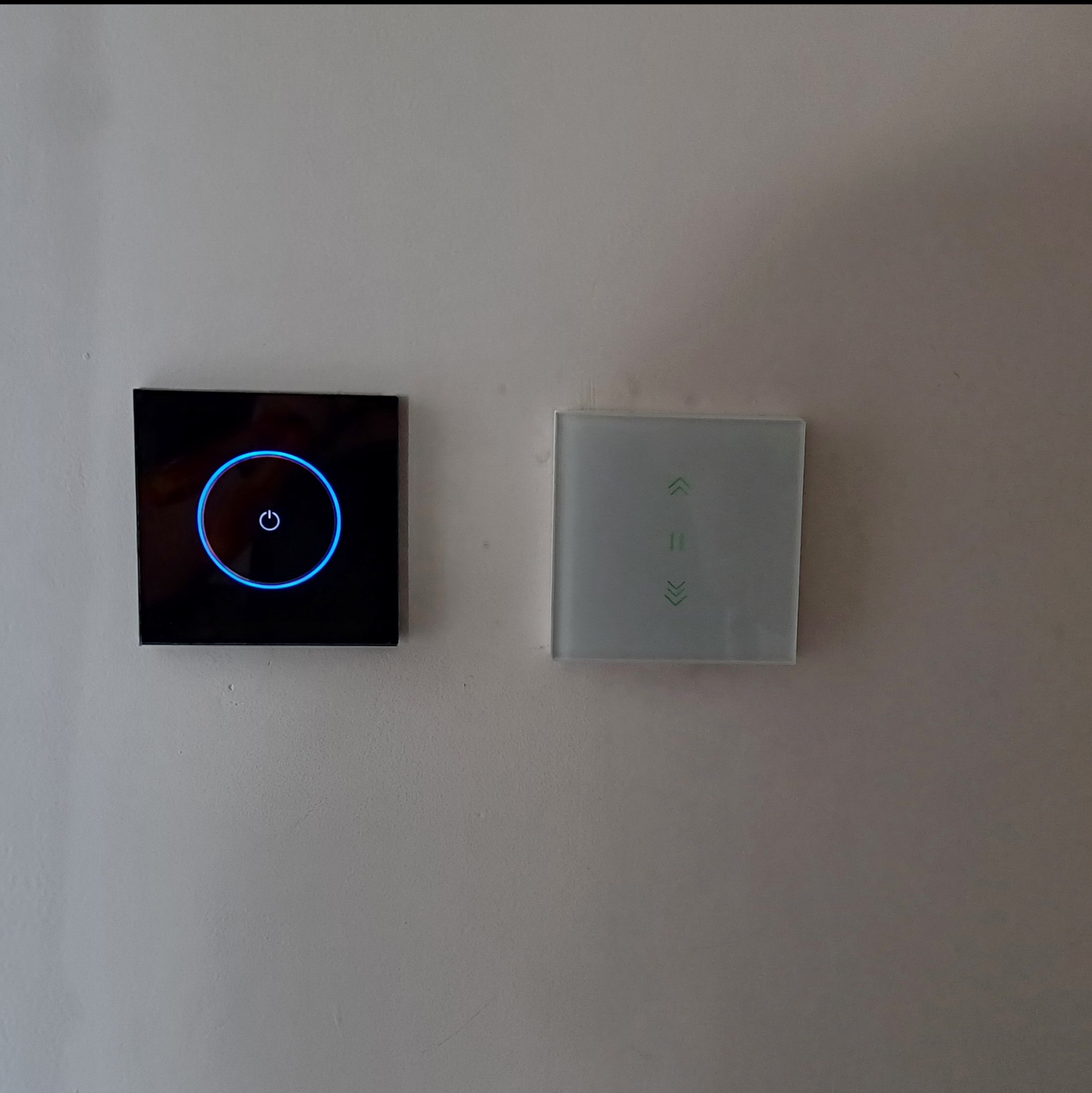 Nowoczesne, dotykowe włączniki światła na ścianie: czarny z podświetleniem LED i biały z symbolami strzałek góra/dół. Minimalistyczny design.