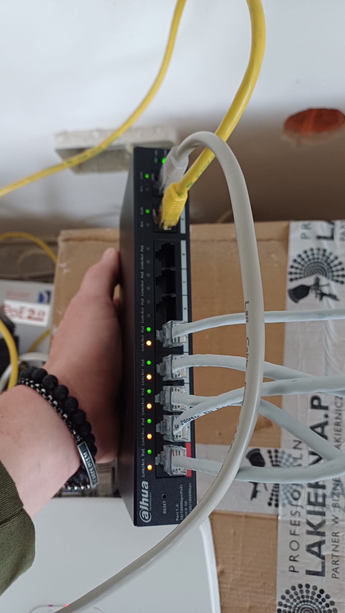 Podłączony switch Dahua z wpiętymi kablami Ethernet, diody LED sygnalizują działanie portów. Widoczna dłoń trzymająca urządzenie.