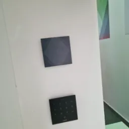 Dwa czarne panele Loxone na białej ścianie, jeden z klawiaturą numeryczną, drugi gładki z subtelnym wzorem. Nowoczesny design, minimalistyczny styl.