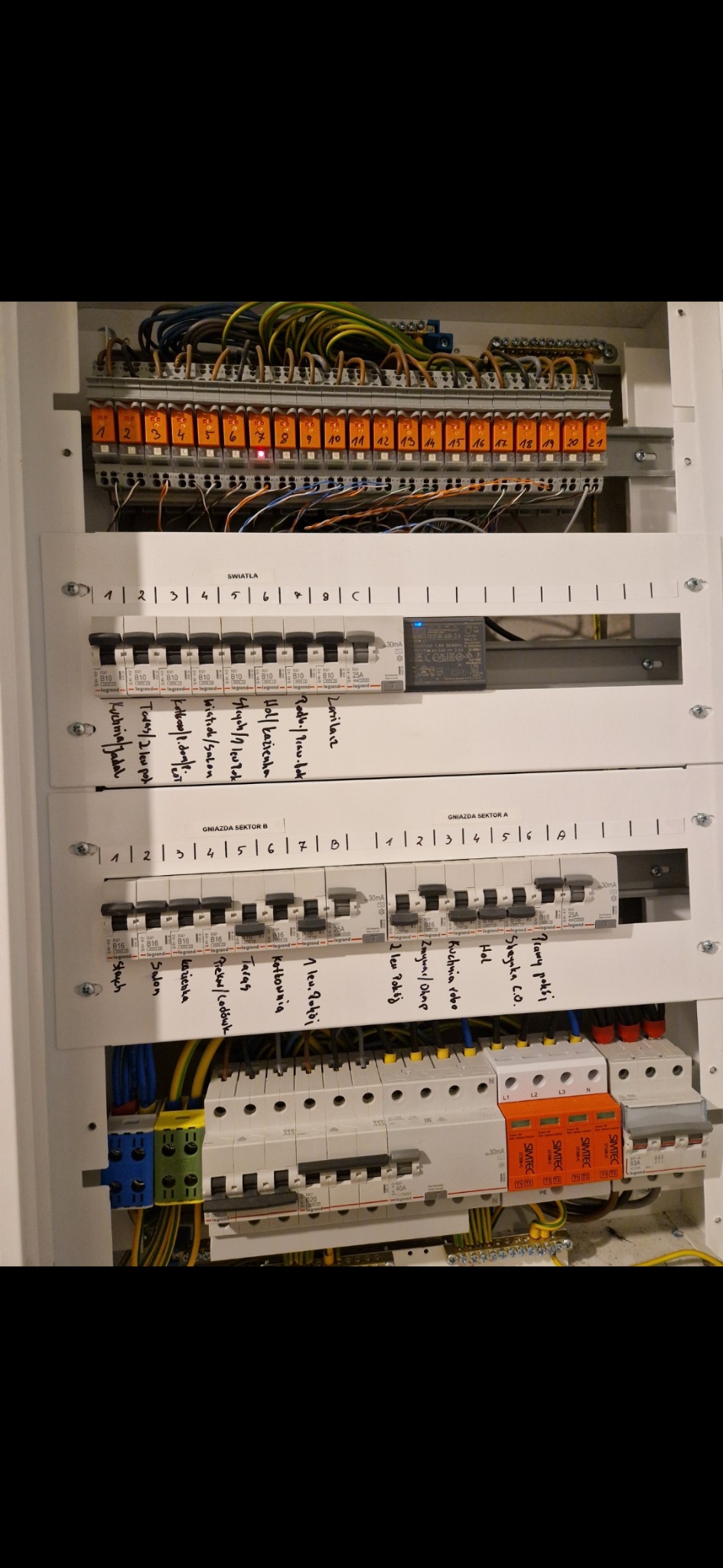 Rozdzielnia elektryczna z bezpiecznikami, opisana odręcznie, widoczne przewody i zabezpieczenia. Element instalacji elektrycznej w domu.