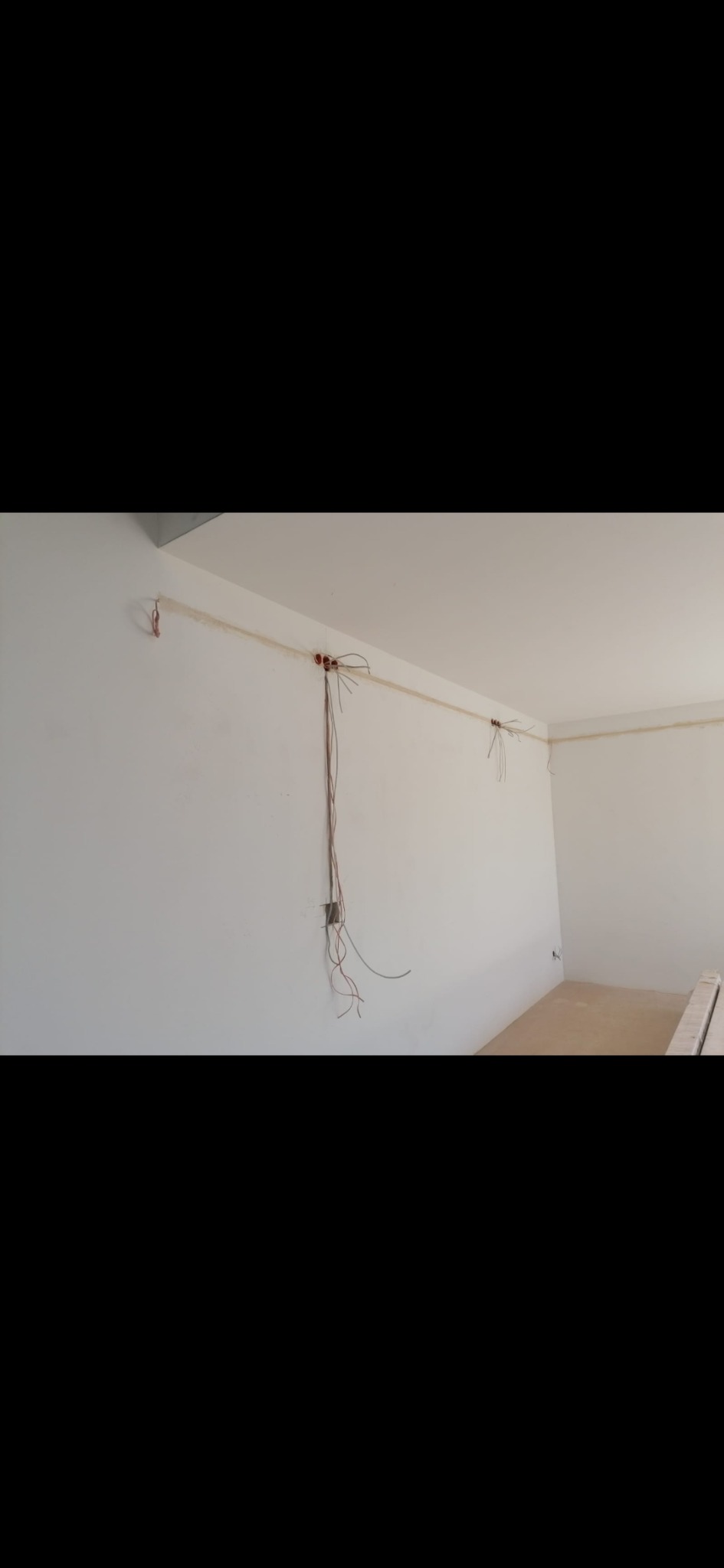 Wnętrze w trakcie prac elektrycznych: przewody wystające ze ściany, puszki instalacyjne. Białe ściany, surowa podłoga. Instalacja elektryczna w nowym budynku.