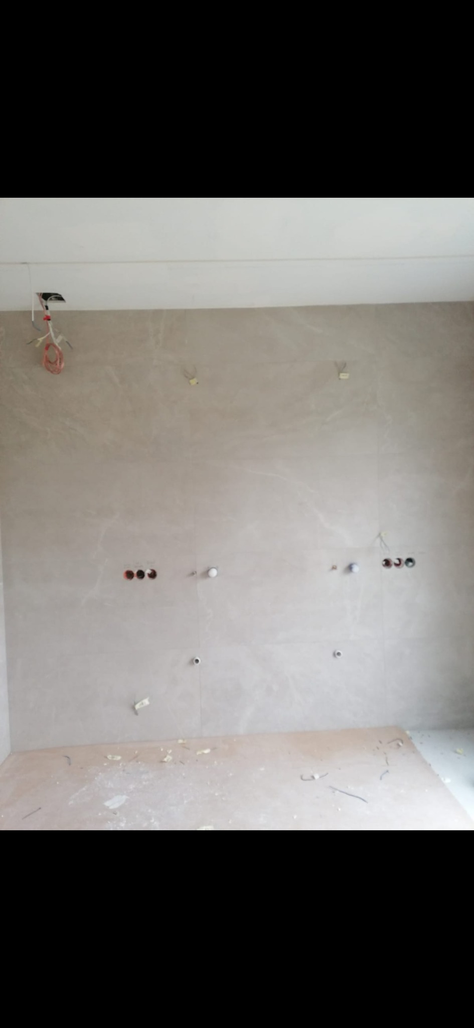 Wnętrze w trakcie prac wykończeniowych. Widoczne wyprowadzone przewody elektryczne i puszki na ścianie wyłożonej płytami imitującymi marmur. Przygotowanie do montażu oświetlenia.